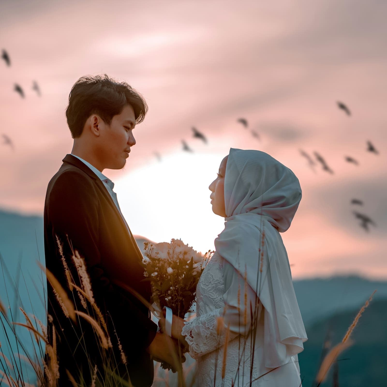 A couple standing together at sunset, holding a bouquet