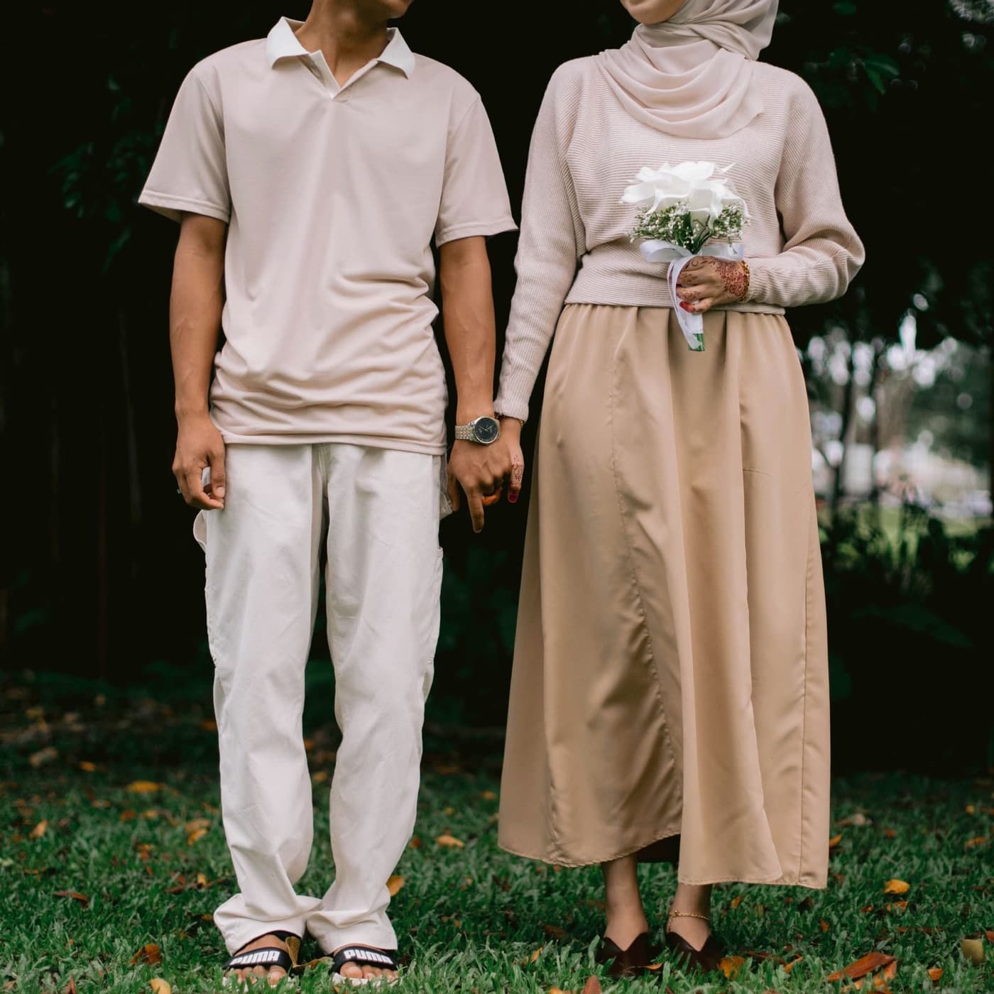 A couple in soft neutral clothes holding hands on a lawn