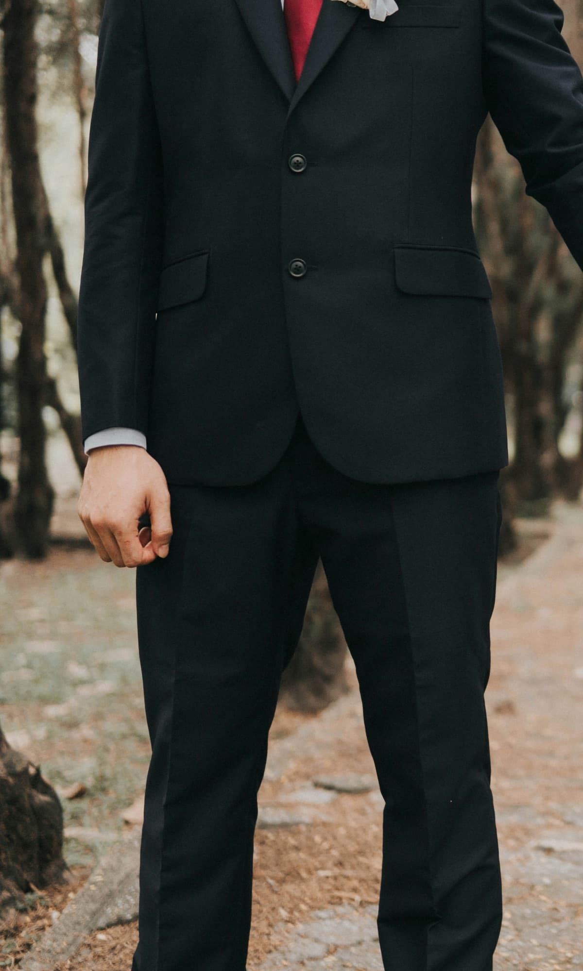 A groom in a dark suit standing on a tree-lined path