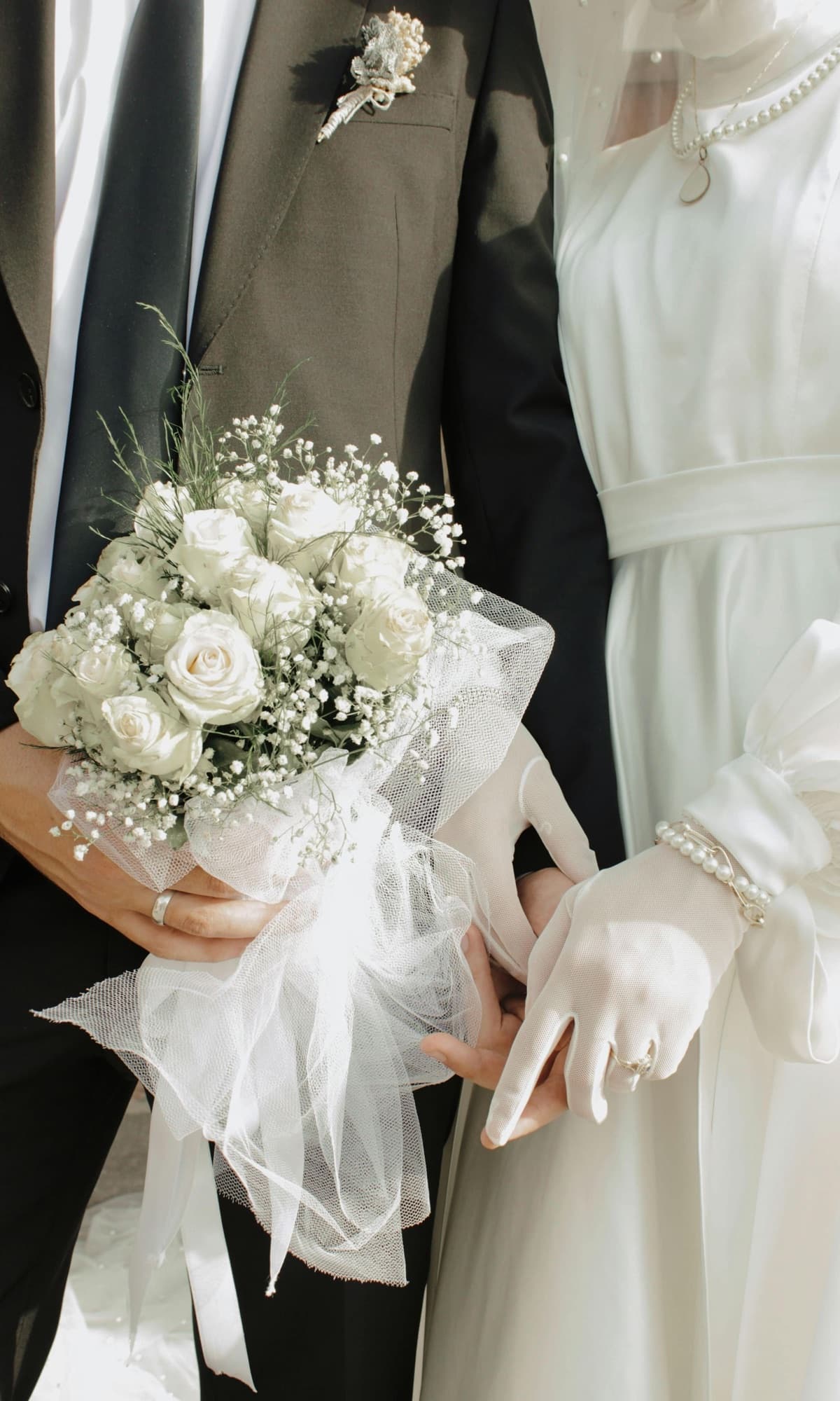 A bride and groom side by side, her bouquet of white roses in her gloved hands